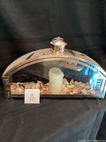Front view of metal and glass arched candle holder displaying candle and seashells