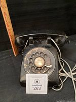 Front view of black rotary telephone showing dial and handset on cradle