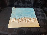 Front view showing square plate with beach scene and seashell relief