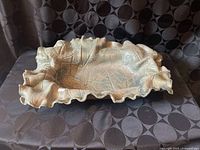 Oblong leaf-impressed stoneware bowl with ruffled edge displayed on fabric backdrop
