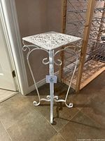Front view of the white cast iron plant stand showing scroll legs and square top