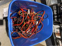 Blue bin holding tangled sets of red, black, and yellow booster cables