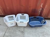 Front view of three plastic laundry baskets lined up: two white square, one blue rectangular