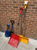 All four shovels standing against brick wall, showing colors, handle types, overall height