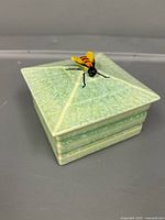 Overall view of closed square green ceramic box with bee handle on lid