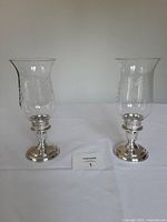 Full view of both silver-plated hurricane candlesticks with glass chimneys