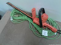 Orange Black & Decker hedge trimmer resting atop coiled green extension cord