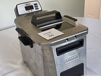 Full view of deep fryer exterior showing stainless housing, lid with window, side handles and DeLonghi logo