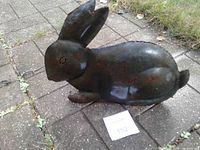 Side view of hollow metal rabbit sculpture on patio block with lot card