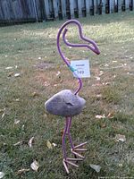 Full view of pink metal flamingo sculpture with rock body standing on lawn