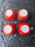 Four red Pyrex #407 mini dishes underside view with coin for scale, showing varying degrees of exterior fading