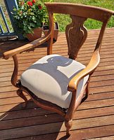 Front angle of carved wood armchair with beige padded seat on deck