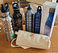 All five stainless water bottles standing with canvas carrier and boxed bottle visible