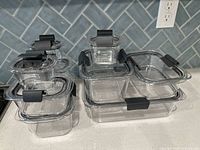 All ten clear plastic containers stacked on countertop showing sizes and black snap-lock lids