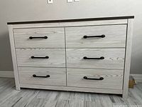Front view of six-drawer dresser showing light gray woodgrain finish, dark top, black pulls
