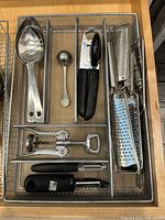 Tray of utensils showing scoops, melon baller, can opener, peeler, corkscrew, graters