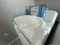 Packaged Liz Claiborne sheet set and white bedding on appliance