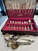 Overview of flatware inside open wood chest plus loose serving utensils