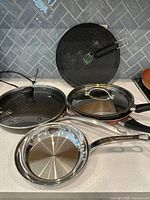 Group view of four KitchenAid pans, two with lids, and splatter screen