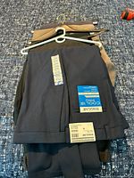 Stack of three new dress pants on hanger showing navy, charcoal, khaki