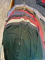 Row of 13 men’s button-down shirts on hangers laid out on bed