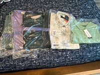 All six shirts laid out on bed, various colors and packaging
