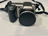 Front view of Olympus SP-500UZ camera with lens cap and strap