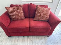 Front view of red loveseat with two patterned pillows