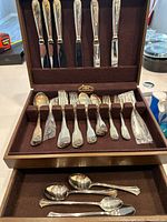 Open flatware chest showing knives in lid, forks and spoons in rack, and teaspoons in drawer