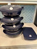 Stack of four round dark blue vented-lid containers beside one rectangular container