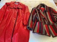 Red vinyl raincoat and striped wool jacket side by side on bed
