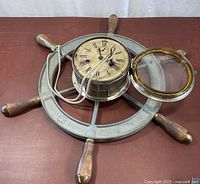 Full view of metal ship’s wheel with clock mounted, bezel open