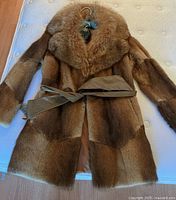 Full view of fox fur coat with leather belt on hanger