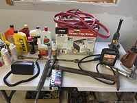 Overall view of table with fridge/warmer box, jumper cables, fluids, tow strap, tools