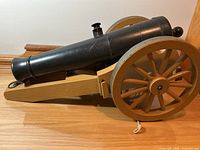 Side view of plastic cannon showing black barrel and tan carriage with spoked wheels
