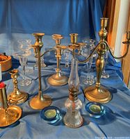 Group view showing brass and silver-tone candelabras, brass candlesticks, oil lamp, blue and clear glass candle holders