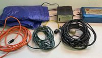 All items laid out: three extension cords, blue tarp, power supply, fence charger