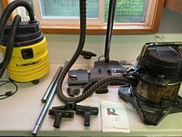 Overall view: Rainbow E Series vacuum, Genie 5-gallon vac, accessories on table