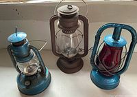 Three kerosene lanterns on sill; two blue, one brown