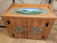 Front view of wood cabinet with painted wreaths and hardware