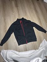 Front view of black Jordan track jacket with red zipper and logo