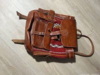 Front view showing leather flap, two front pockets, woven textile panel
