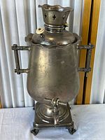 Front view of metal samovar showing body, handles, spigot, pedestal base