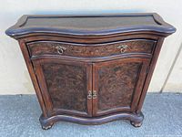 Front view of serpentine wood cabinet showing drawer, doors, hardware, veneer