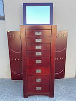 Front view of dark cherry jewelry armoire with side doors open, drawers closed, mirror lifted