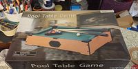 Front of unopened box showing mini pool table game image and accessories