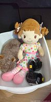 Overall view of cloth baby doll, brown plush animal, and black Build-A-Bear shoes in bin