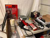 Assorted automotive items on table including K&N filter, trouble light, grease gun, tire inflator, decals