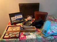 All twelve items arranged on floral table: magnifier box, baseball, porcelain ashtray, gavel, open manicure set, Seiko watch, binocular case, phone, notebook, sunglasses cases