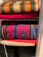 Shelf with three folded wool blankets showing plaid, solid red and multicolour striped examples